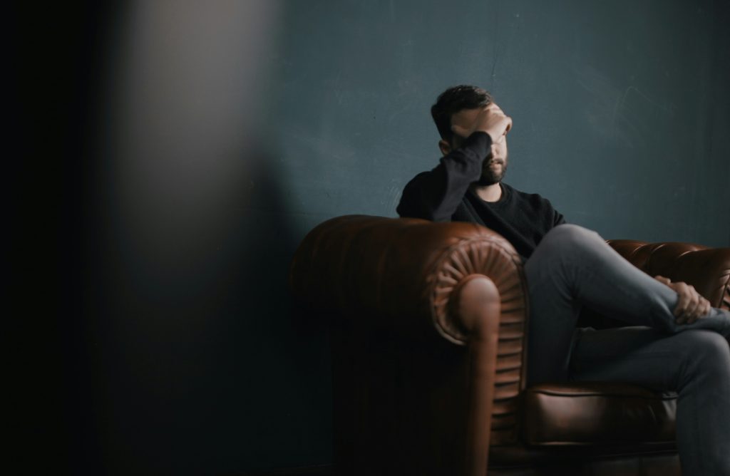 Man in counseling sitting on a couch with his hand on his forehead 